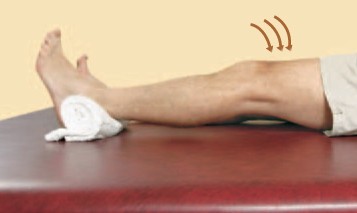 A person lies on a flat surface with one leg extended and a rolled towel under their knee, lifting their lower leg upward as indicated by three curved arrows.