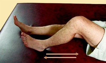 A person lying on a mat with one knee bent and one leg extended, sliding the heel of the extended leg along the surface; a double-headed arrow indicates movement back and forth.