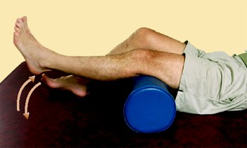 A person lies on their back with knees slightly bent, one lower leg resting on a blue foam roller. Arrows show the person lifting and lowering their foot, demonstrating a leg exercise.