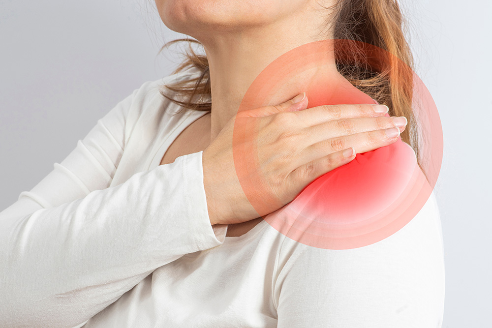 A woman wearing a white shirt holds her left shoulder, which is highlighted with a red circular area, indicating pain or discomfort.