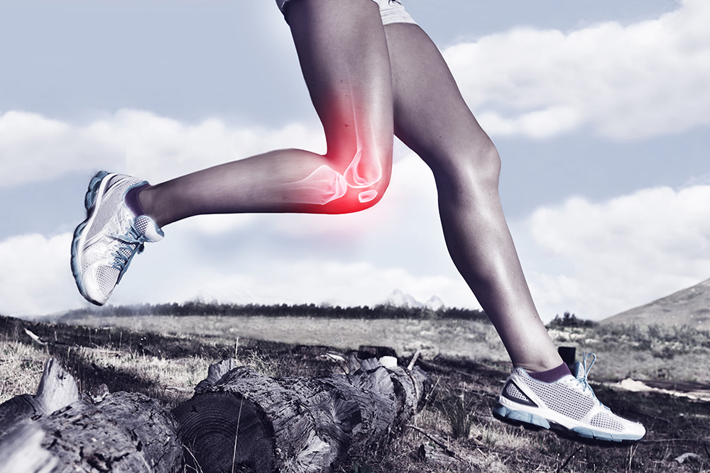 A person running outdoors, with a digital illustration highlighting knee pain or injury in red on their right leg. The background shows logs on the ground and mountains in the distance.