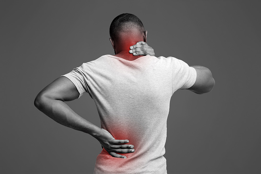 A person holding their neck and lower back, both highlighted in red to indicate pain or discomfort, on a gray background. The person is facing away from the camera and wearing a light gray t-shirt.