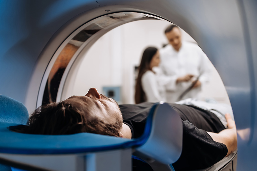 A person lies inside an MRI scanner, viewed from the machine’s opening, while two medical professionals stand in the background discussing results.
