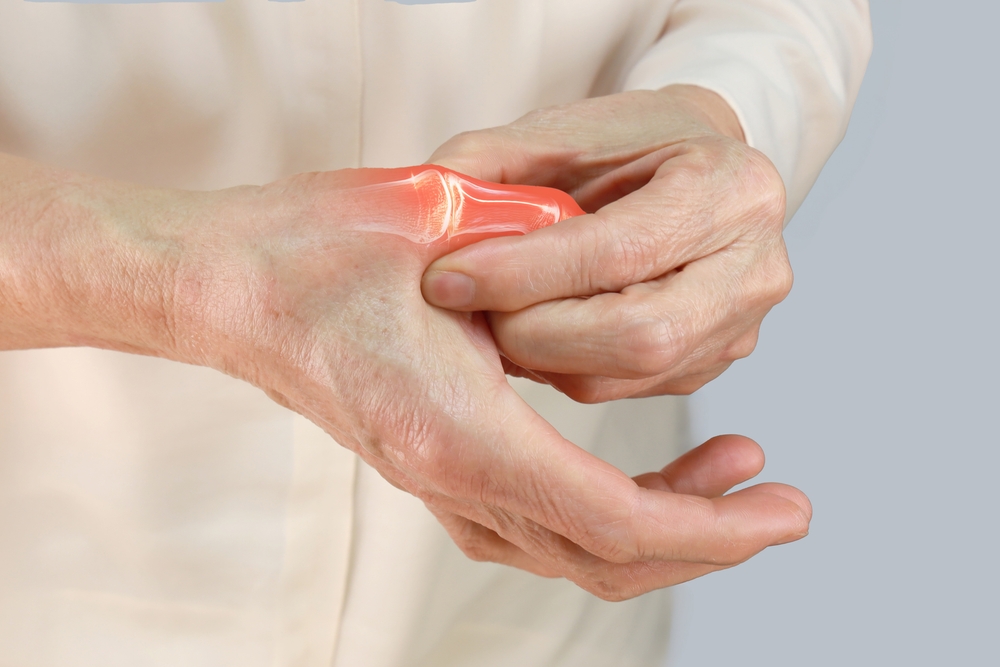 An elderly person holding their painful thumb joint, with a digital red highlight emphasizing the affected joint, suggesting pain or arthritis. The background is plain and neutral.