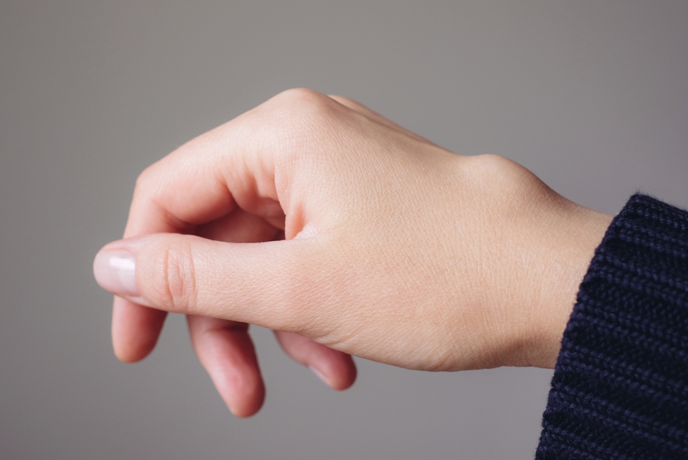 A close-up of a persons left hand and wrist against a plain background, with the hand slightly curved and the person wearing a dark, ribbed sleeve.