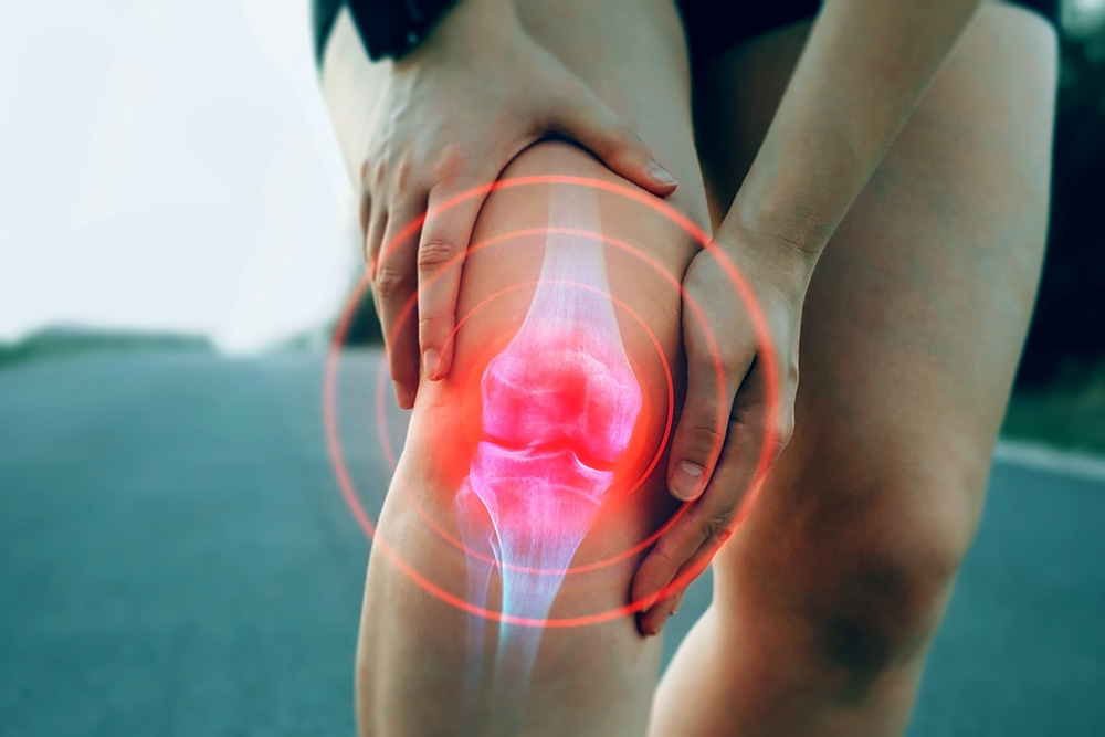 A person clutching their knee in pain with a digital overlay showing the knee joint and red concentric circles, emphasizing pain or injury in the knee area.
