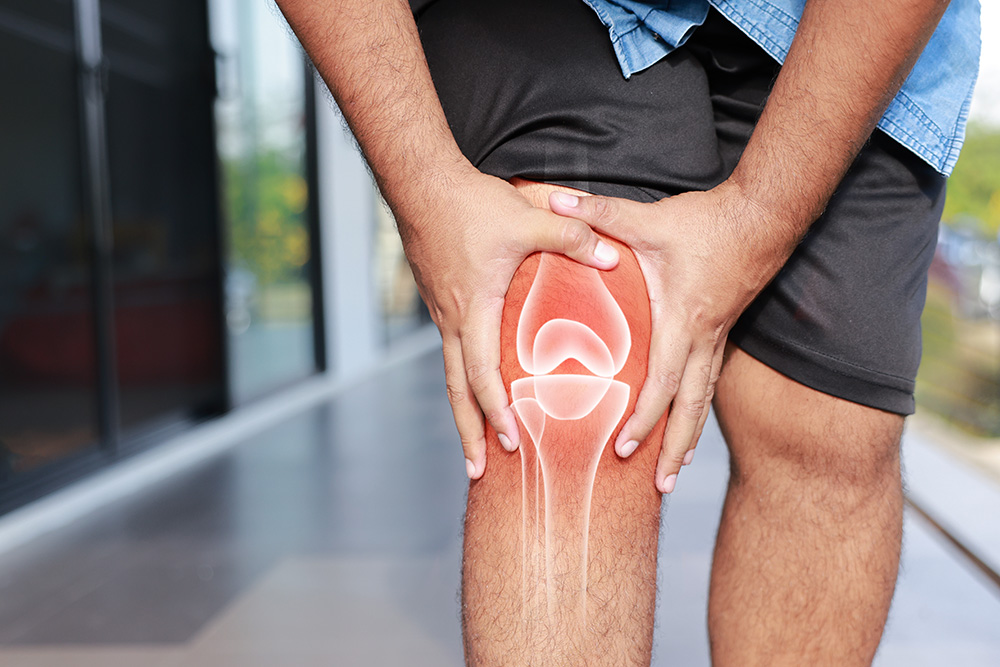 A person holding their knee in pain, with a digital illustration of the knee joint anatomy and bones superimposed on the leg, indicating discomfort or injury.
