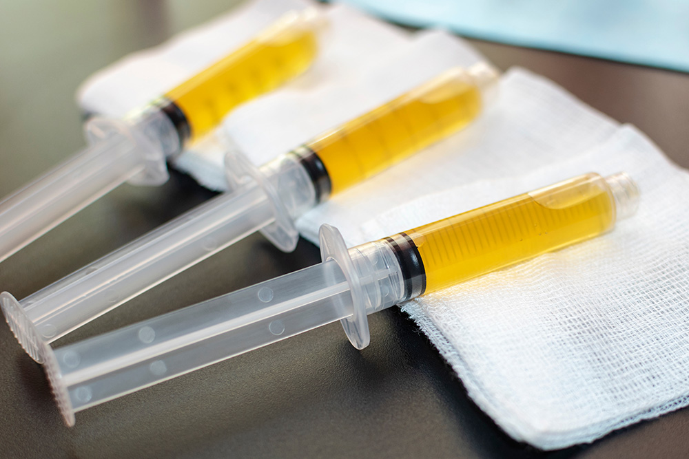 Three syringes filled with yellow liquid rest on white medical gauze pads, placed on a dark surface.