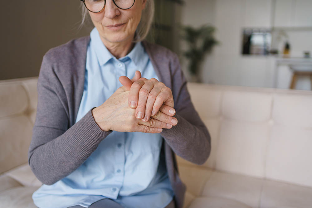 An older woman with glasses is rubbing her hands together.