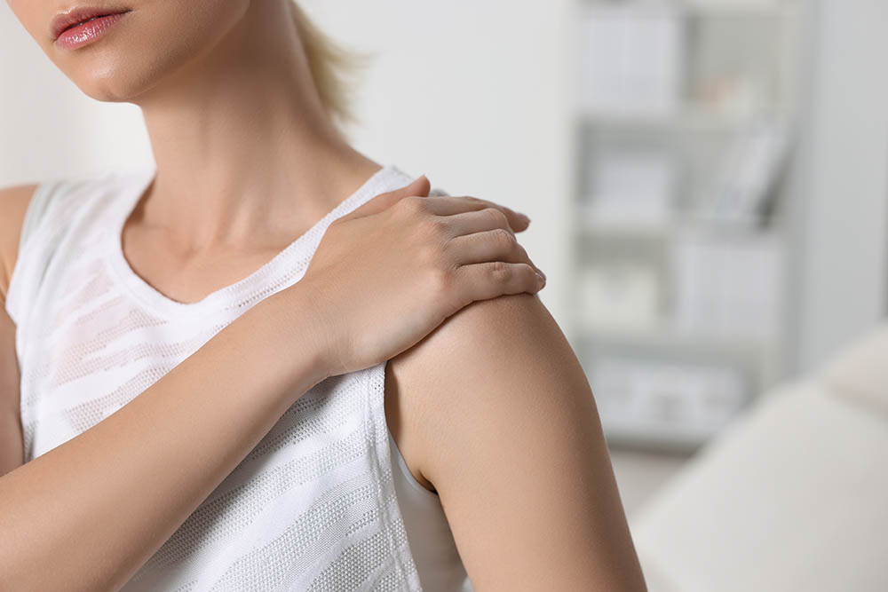 Close-up of a womans shoulder with her hand resting on it. She is wearing a white tank top.