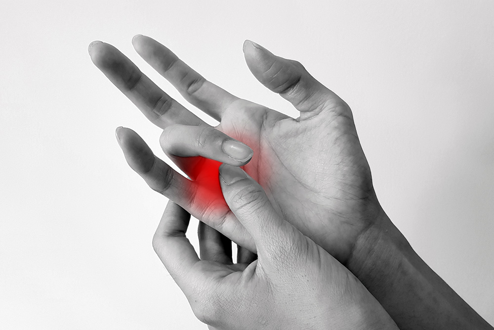 A person pressing the base of their finger with their other hand; the area is highlighted in red, suggesting pain or discomfort.